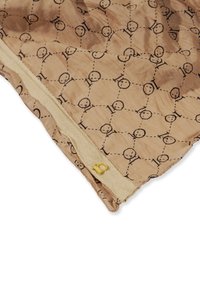 Lysbeige stof med et gentagende sort geometrisk mønster. Har en beige lynlås med en lille gul figur '10' accent.