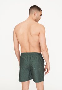 Vihreät kuviolliset uimashortsit, joissa on joustava vyötärö, takatasku ja väljä malli, nähtynä takaa.