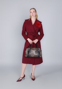 Burgundyröd omslagsoverall med knytliv, en röd fjäderaccent, i kombination med en leopardmönstrad handväska och burgundy pumps med ankelsnörning.