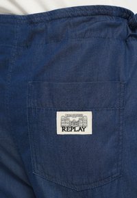 Σκούρο μπλε τζιν παντελόνι με πίσω τσέπη που φέρει ραμμένη λευκή ετικέτα με την επιγραφή "REPLAY" και διακοσμητικές λεπτομέρειες. Ομαλή υφή.