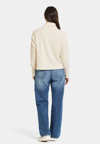 Krämfärgad, fluffig fleece-pullover med hög krage, kort design och långa ärmar, kombinerad med blå, löst sittande jeans.