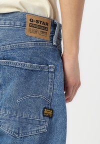 Blauwe denim jeans met een leren logo patch op de achterband en een zwart stoffen label. Heeft contrasterende stikken en klassieke achterzakken.