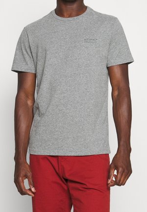 Grijs katoenen T-shirt met een ronde hals, korte mouwen en een klein logo op de borst gedrukt. Gecombineerd met een rode broek.