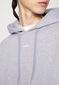 Sudadera gris con cordones metálicos y logo blanco "SANDRO". Fabricada en algodón con una textura suave, cuenta con capucha y un corte relajado.