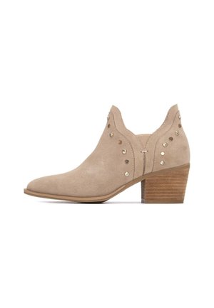 Stivaletto alla caviglia in camoscio beige con punta affusolata, dettagli decorativi con borchie sui lati e tacco impilato in legno.