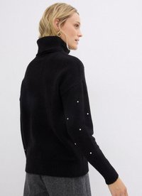 Maglione a collo alto nero con lavorazione a maglia testurizzata, punteggiato da accenti di perle sulle maniche, presenta una vestibilità morbida e bordo a costine.