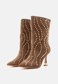 Botas de tobillo de ante marrón con punta afilada, adornadas con acentos de perlas y patrones en forma de ola, con un alto tacón de aguja.