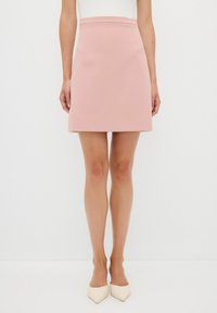 Mini falda rosa en tejido estructurado, con cintura ajustada y corte recto, combinada con tacones de punta crema.