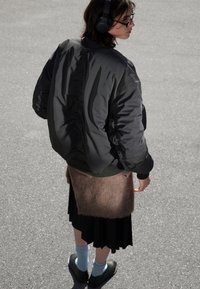 Musta pommikapakka, jossa on kerätty takaosa, vaaleanruskea tekoturkishame, musta laskostettu hame, siniset sukat ja mustat kengät harmaalla pinnalla.
