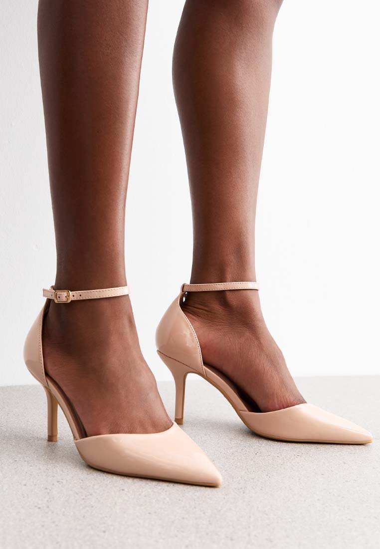 Nude lakleren hoge hakken met een spitse neus, enkelschoenen en een gladde textuur, tegen een neutrale achtergrond.