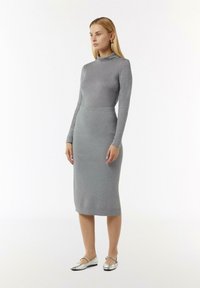 Grijze aansluitende jurk met lange mouwen en hoge kraag, gemaakt van zacht materiaal, gecombineerd met glanzende zilveren ballerina's. Eenvoudig, gestroomlijnd ontwerp.