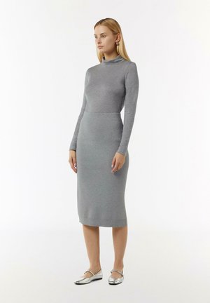Grijze aansluitende jurk met lange mouwen en hoge kraag, gemaakt van zacht materiaal, gecombineerd met glanzende zilveren ballerina's. Eenvoudig, gestroomlijnd ontwerp.