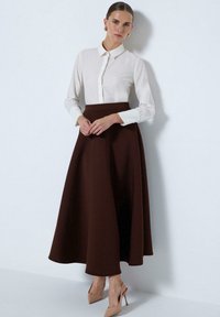 Brown midi skirt with a flared silhouette paired with a white long-sleeve button-up shirt. Features soft fabric and minimalistic design.