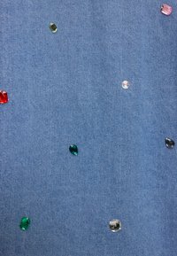 Spijkerstof met verspreide, kleurrijke namaakstenen in rood, roze, groen en transparant, die een textuurrijk en decoratief uiterlijk creëren.