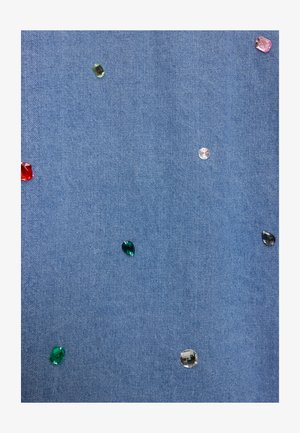 Tissu en denim orné de fausses pierres colorées dispersées en rouge, rose, vert et transparent, créant un aspect texturé et décoratif.