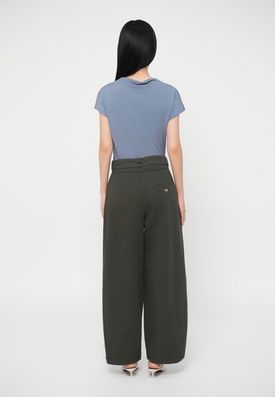Μπλε κοντομάνικο μπλουζάκι και ψηλόμεσες, φαρδιές ελαιοπράσινες παντελόνες με ορατή πίσω τσέπη και μια μικρή λογότυπη λεπτομέρεια.
