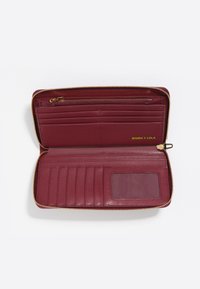 Bordowy skórzany portfel z złotym zamkiem błyskawicznym, wieloma kieszeniami na karty, jednym przezroczystym oknem na identyfikator oraz gładką fakturą. Nazwa marki widoczna wewnątrz.