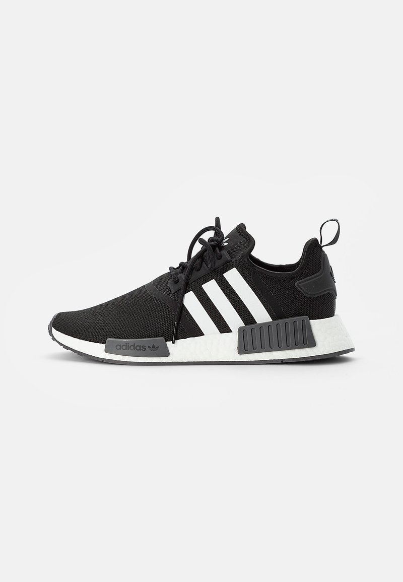 Chaussure de sport noire avec un dessus en tricot, trois bandes blanches, semelle en caoutchouc et contrefort texturé. Dispose d'un intercalair en mousse blanche.