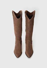 Brown suede knee-high boots with pointed toes, featuring decorative stitching and a scalloped design, open at the top for easy wear.