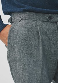 Grau gemusterte Hose aus strukturiertem Stoff, mit taillierter Passform, seitlichen Taschen und einer Metallschnalle zur Verstellung des Bundes.