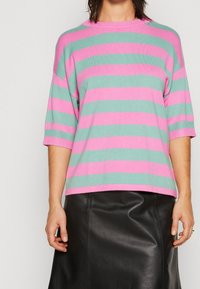 Pull en maille rayé avec des bandes horizontales vert clair et rose, col rond et manches larges, associé à une jupe en cuir noire.