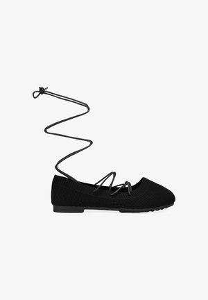 Zapato plano de ballet de punto negro con tiras cruzadas y cordones largos que se extienden hacia arriba en forma de espiral.