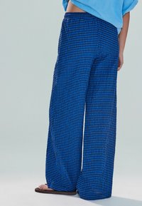 Pantalon large à carreaux bleus et noirs avec une coupe décontractée et une taille élastique, fabriqué en tissu léger, présentant une texture lisse.