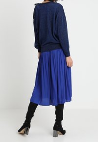 Merino villasta kudottu tummansininen neulepaita, jossa on löysä malli ja textured pinta. Se on yhdistetty virtaavaan siniseen hameeseen ja mustiin polvenyli saappaisiin.