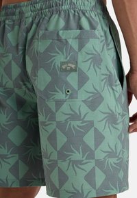Costum de baie verde cu un design geometric, având forme de diamant și modele stilizate de plante. Talie elastică și buzunare laterale.
