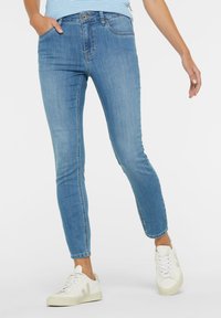 Light blue skinny jeans made of denim, featuring five pockets, a zip fly, and a faded finish. Paired with white sneakers.