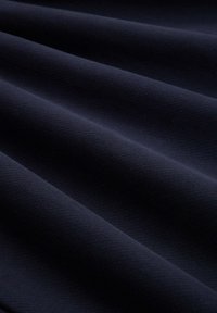 Marininblått tyg med en mjuk struktur, försedd med mjuka, diagonala veck som skapar djup och en rik framtoning.