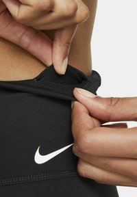 Leggings sportivi neri con una vita testurizzata. Un logo Nike bianco è ben in vista. Mani che sistemano la vita.