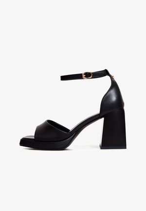 Schwarze High-Heelsandale mit einem glatten Lederoberteil, offenen Zehen, einem Knöchelriemen mit goldenem Schnallenverschluss und einem stabilen Blockabsatz.