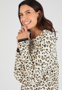 Felpa a stampa leopardata in crema con accenti neri e dorati. Caratterizzata da polsini a coste e un taglio morbido, che mette in risalto un tessuto testurizzato.