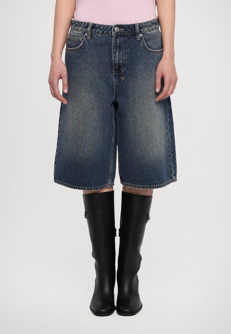 Denima culottes ar platām kājām, vidējā izmazgājumā un nolietotu malu, kombinētas ar augstām melnām gumijas zālēm, kurām ir elegants dizains un sānu detaļas.