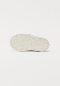 Sneakersåle med et teksturert hvitt gummimateriale, som har et flatt design, synlige dekkmønstre og et lite rektangulært detalj.