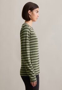 Groene gestreepte lange mouwen shirt met een V-hals en zachte textuur, met horizontale donkere en lichte strepen. Draagt het met zwarte broek.