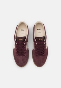 Burgundy suede sneakers with cream accents, round toe, and flat laces. Gold "BOSS" logo on the tongue and side, rubber outsole.