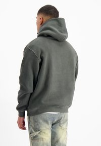 Olijfgroene hoodie met een grote capuchon, geribde manchetten en een ontspannen pasvorm, gecombineerd met lichtgekleurde cargobroeken. Zachte, gestructureerde stof.