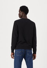 Svart bomullssweatshirt med lange ermer, rund hals og ribbestrikkede mansjetter; kombinert med blå denimjeans med baklommer.
