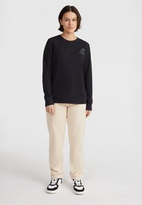 Black long-sleeve shirt with a chest graphic, light beige cargo pants, and black sneakers with white accents. Simple, casual style.