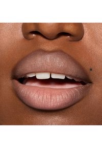 Gros plan sur des lèvres à la texture lisse et mate ; couleur nude clair ; lignes naturelles visibles et un petit point noir sur la lèvre inférieure.