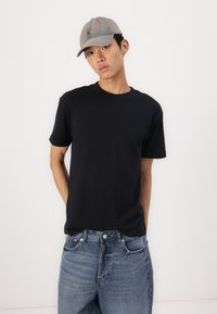 Svart bomull T-skjorte med korte ermer, sammen med lyseblå denimjeans. Kappen er lys grå med en liten logodetalj.