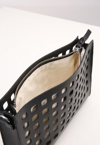 Černá kožená taška s vyřezávanými čtvercovými vzory, vybavená krémovou podšívkou a stříbrným zipem na horní straně.