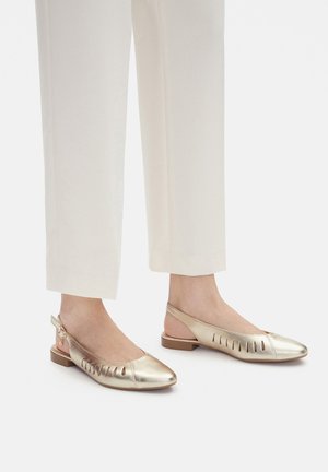 Ballerine slingback in metallo dorato con aperture decorative. Punta arrotondata, tacco basso a blocco e cinturino slingback con fibbia regolabile.