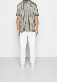 Camiseta gris con efecto tie-dye de manga corta y corte relajado, combinada con pantalones blancos de pierna recta, ambos con elementos de diseño minimalistas.