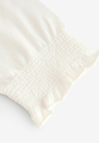 Witte stof met een zachte textuur, voorzien van gegroepeerde smocking en een gerimpelde rand. Het ontwerp is eenvoudig en elegant, met nadruk op comfort.