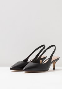 Czarne skórzane szpilki z paskiem za piętą, z wąskim noskiem, cienkim obcasem i minimalistycznym wzornictwem. Gładka faktura z subtelnym połyskiem.