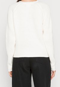 Suéter blanco de punto acanalado con mangas raglán, cuello barco y dobladillo ajustado, combinado con pantalones negros de corte holgado.