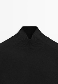 Maglione a collo alto nero realizzato in morbido tessuto a costine. Presenta un collo alto con un leggero taglio a V, una superficie liscia e senza motivi visibili.